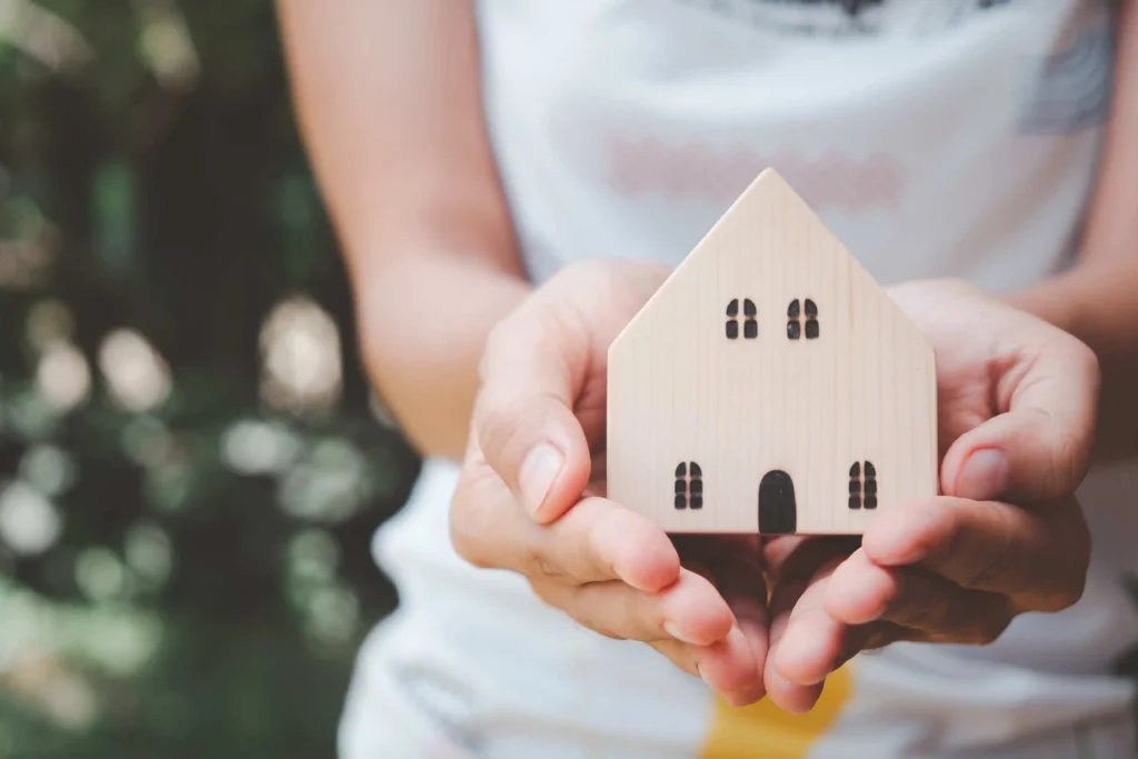 Woman holding wooden house for home protection concept.