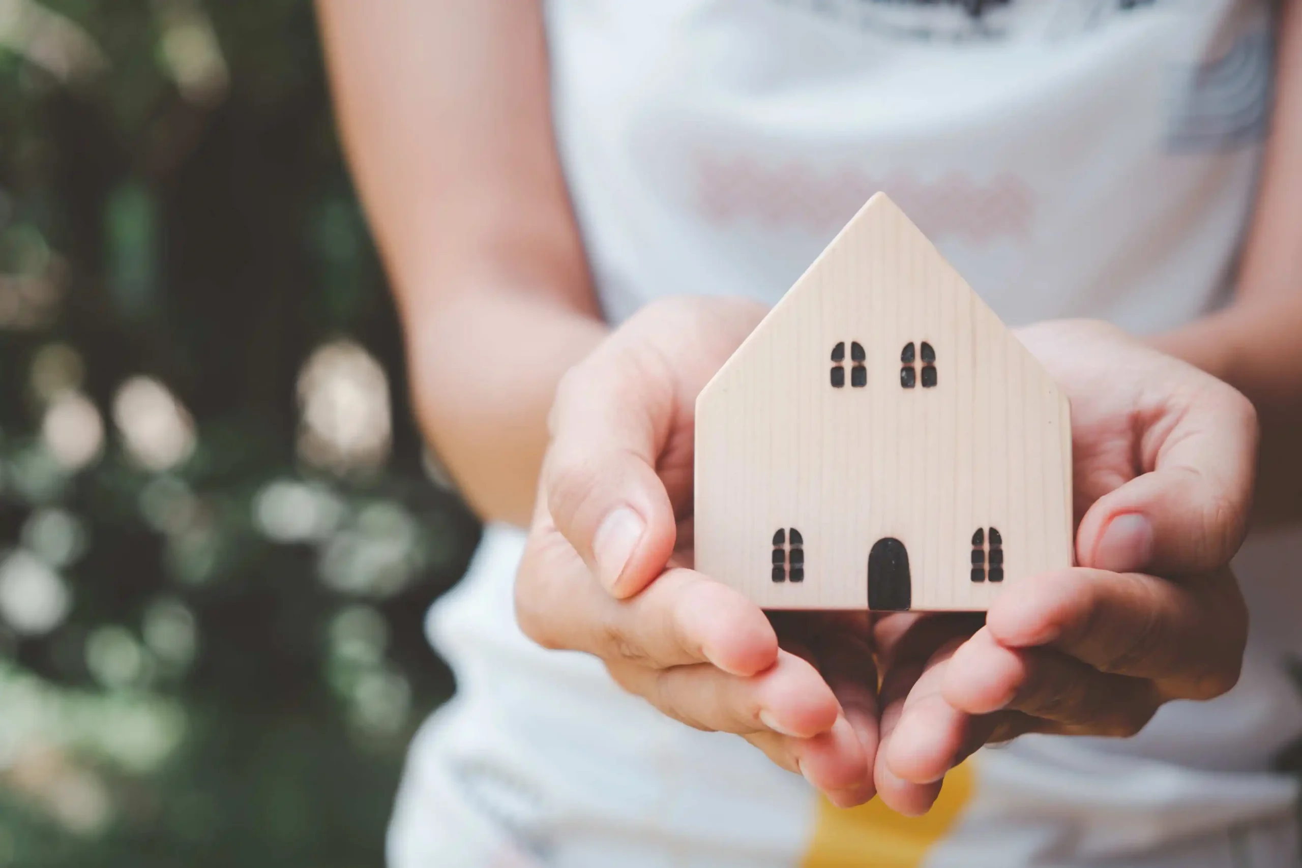 Woman holding wooden house for home protection concept.